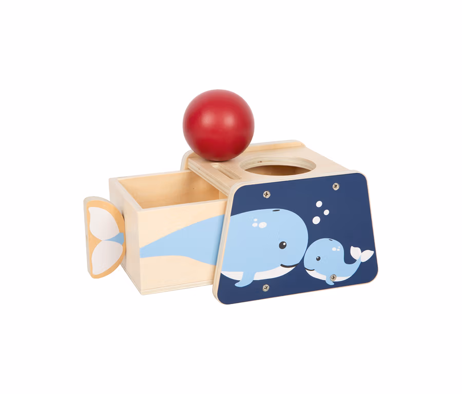 small foot Baby-Box für 10–12 Monate, aus Holz mit rotem Ball und Wal-Illustrationen. Die naturfarbene Box hat eine dunkelblaue Front mit zwei hellblauen Walen. Ein roter Holzball liegt oben in einer Rille, eine Schublade ist links geöffnet.