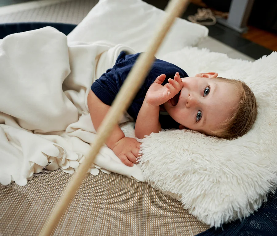 Ein Baby liegt in einer HUDORA Nestschaukel »Lounge«, midnight, Ø 110 cm und HUDORA Nestschaukel »Lounge«, midnight, Ø 90 cm, zugedeckt mit einer Decke.