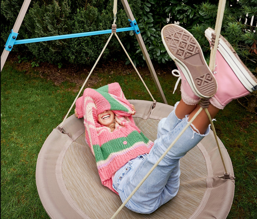 Eine Frau liegt in der beigen HUDORA Nestschaukel »Lounge«, Ø 110 cm und lacht.