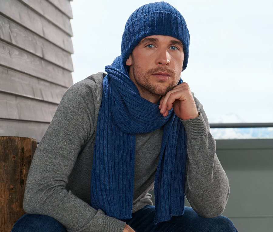 Mann sitzt mit Strickschal und Mütze.