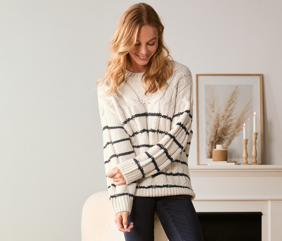 Frau trägt einen gestreiften Strickpullover, Jeans und Stiefel.