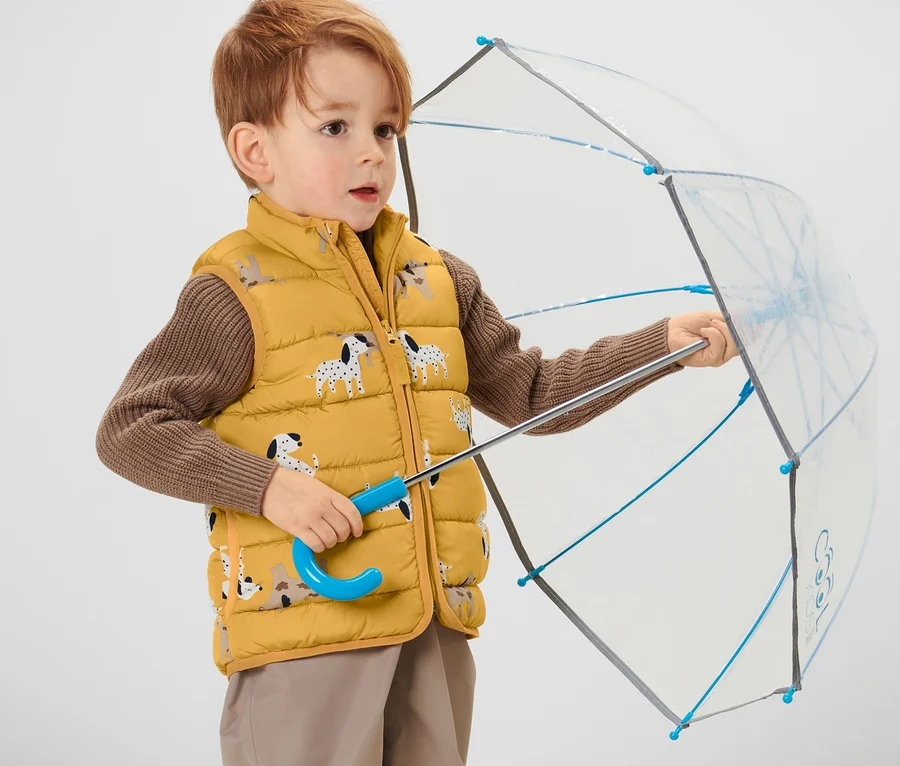 Junge hält geöffneten Regenschirm und trägt eine Kinder-Steppweste.