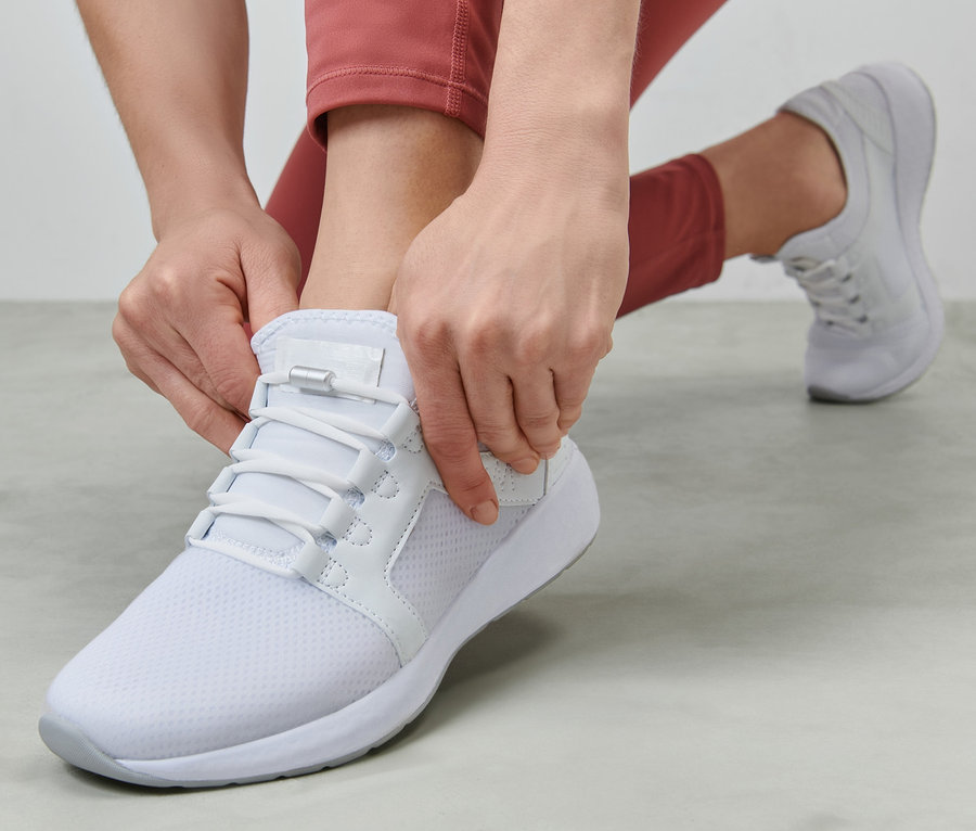 Frau schließt elastische Schnürsenkel an einem weißen Schuh.