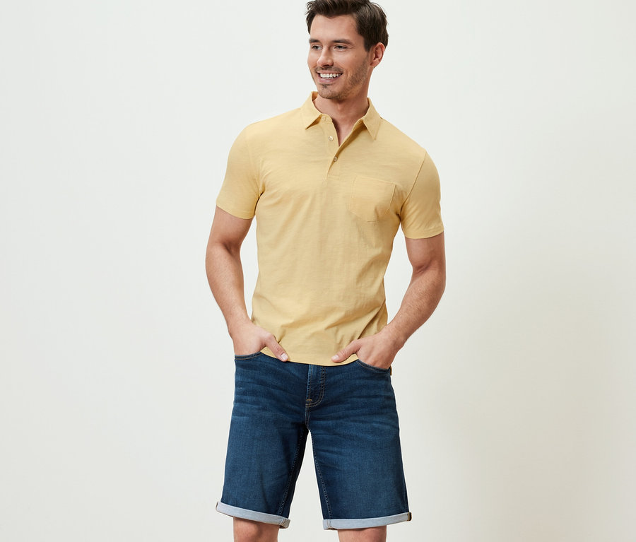 Mann posiert in gelb meliertem Jersey-Poloshirt und Jeansshorts.