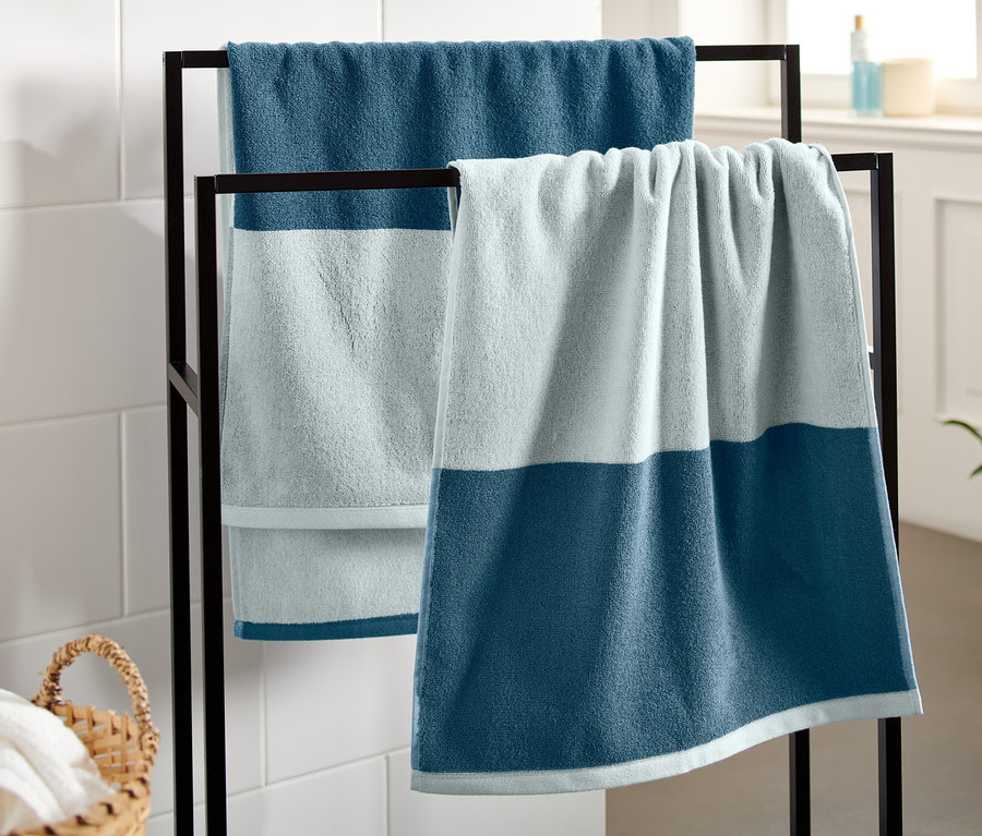 Zwei blaue Jacquard-Handtücher hängen auf einem schwarzen Ständer im Badezimmer.