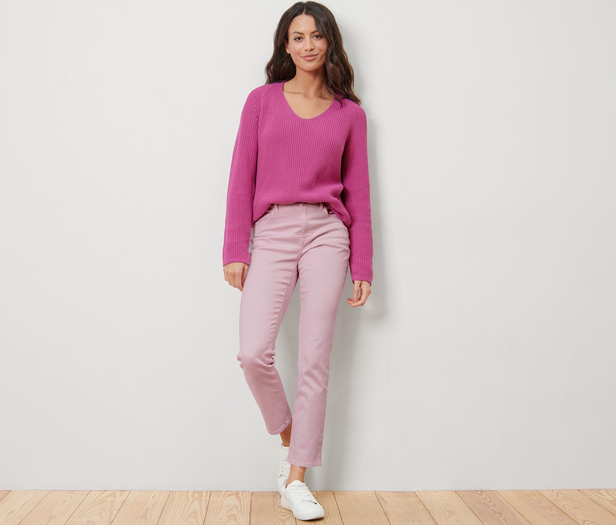 Eine Frau steht und trägt eine rosafarbene Jeans – Fit »Emma« und einen lila Pullover.