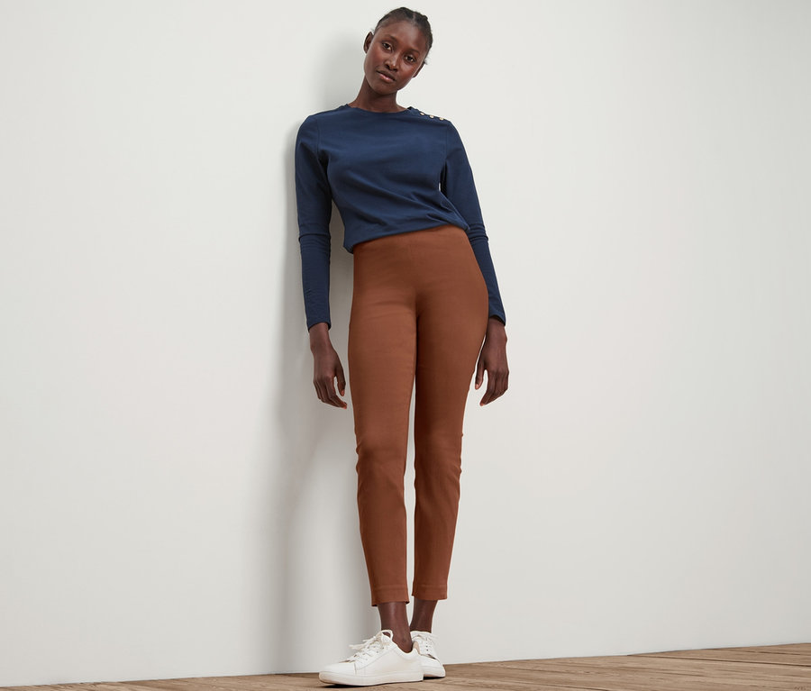 Frau posiert in cognacfarbener Stretchhose und blauem Oberteil.