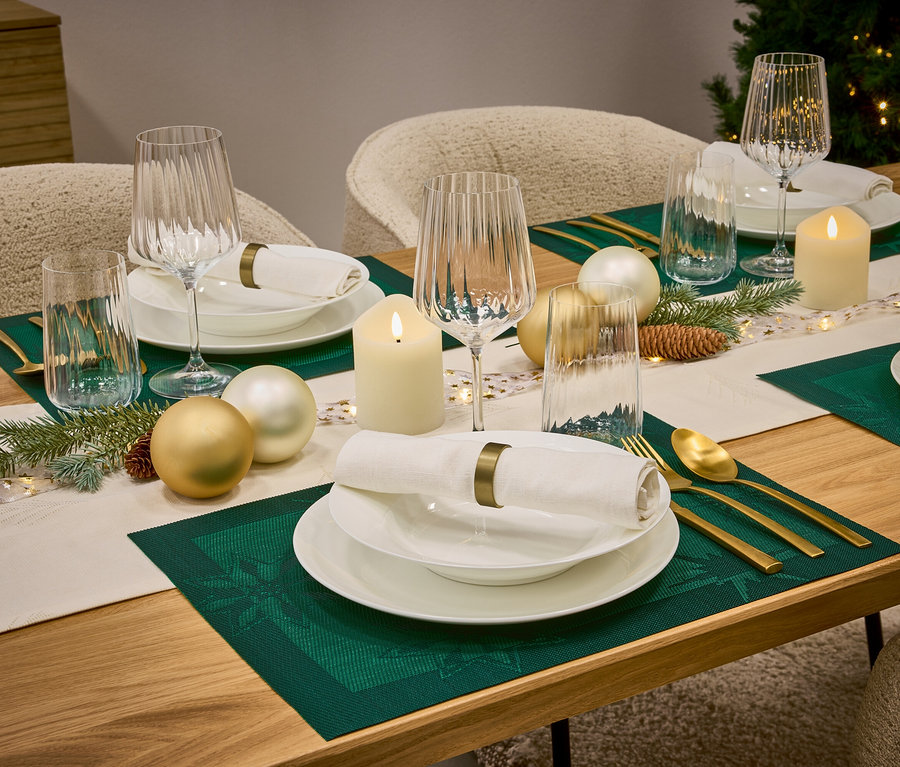 Ein gedeckter Tisch mit weißem Geschirr, Gläsern, goldenem Besteck, grünen Tischsets und Weihnachtsschmuck.