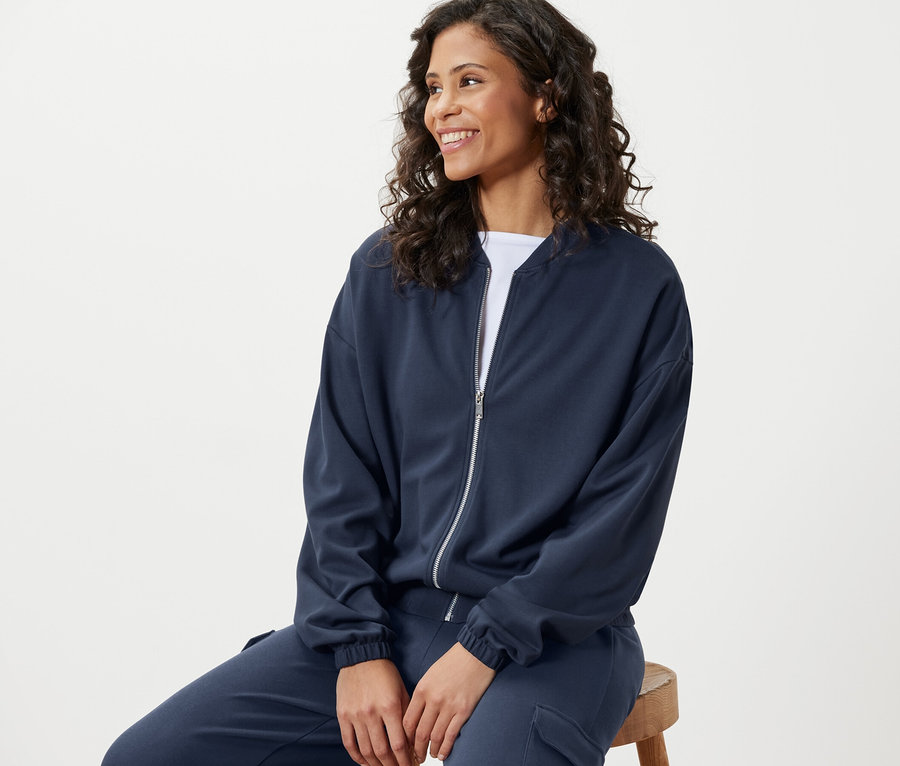 Frau sitzt und trägt eine blaue Sweatjacke.