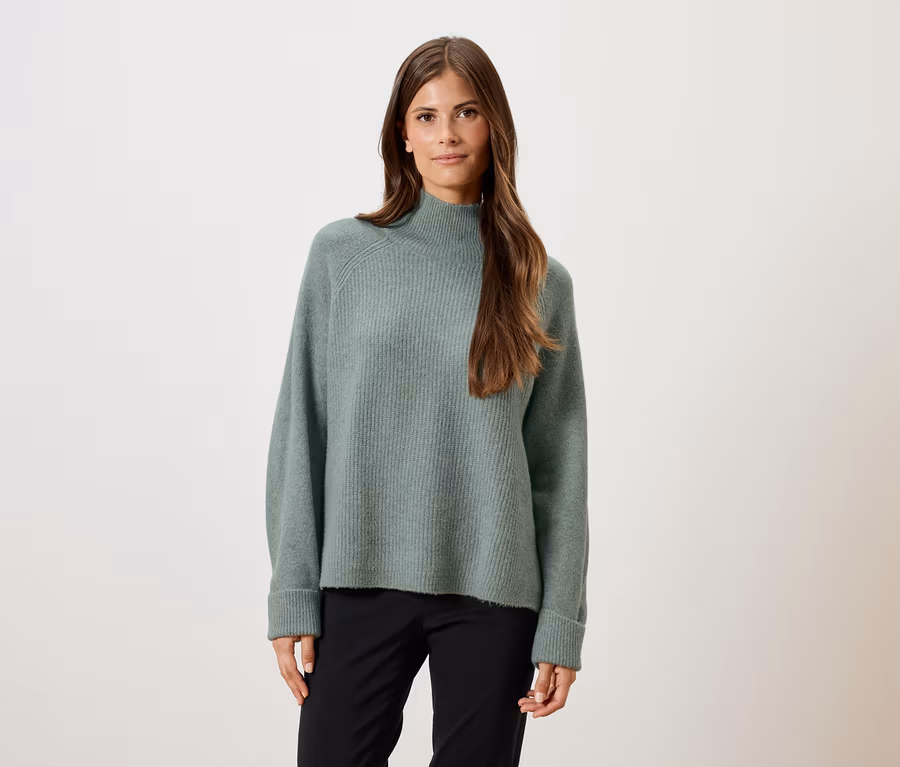 Frau trägt einen grünen Pullover und eine schwarze Hose.