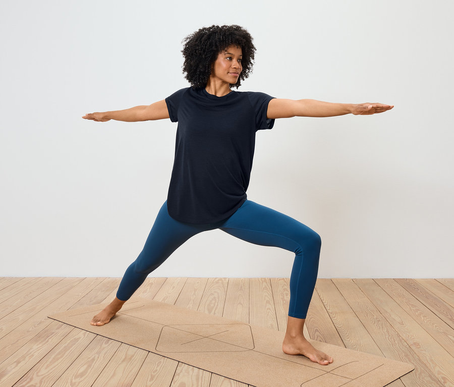 Frau in blauen Leggings und schwarzem T-Shirt macht Yoga auf einer Matte.
