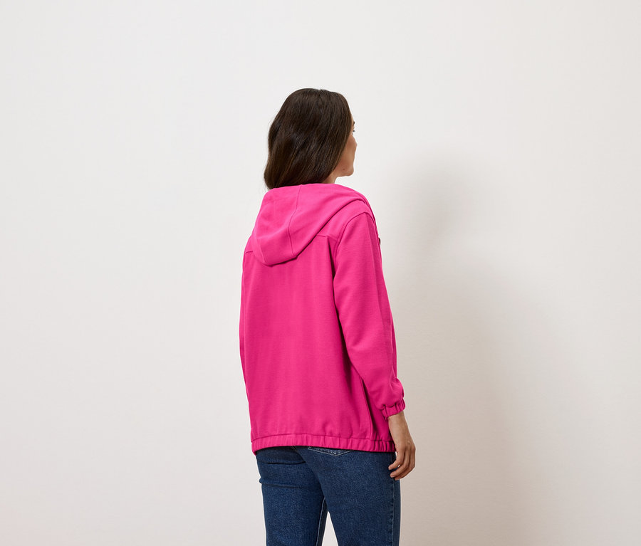 Frau mit dem Rücken zur Kamera trägt einen pinkfarbenen Hoodie und blaue Jeans.