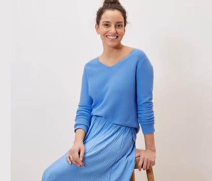 Frau sitzt auf einem Hocker und trägt einen hellblauen Strickpullover.