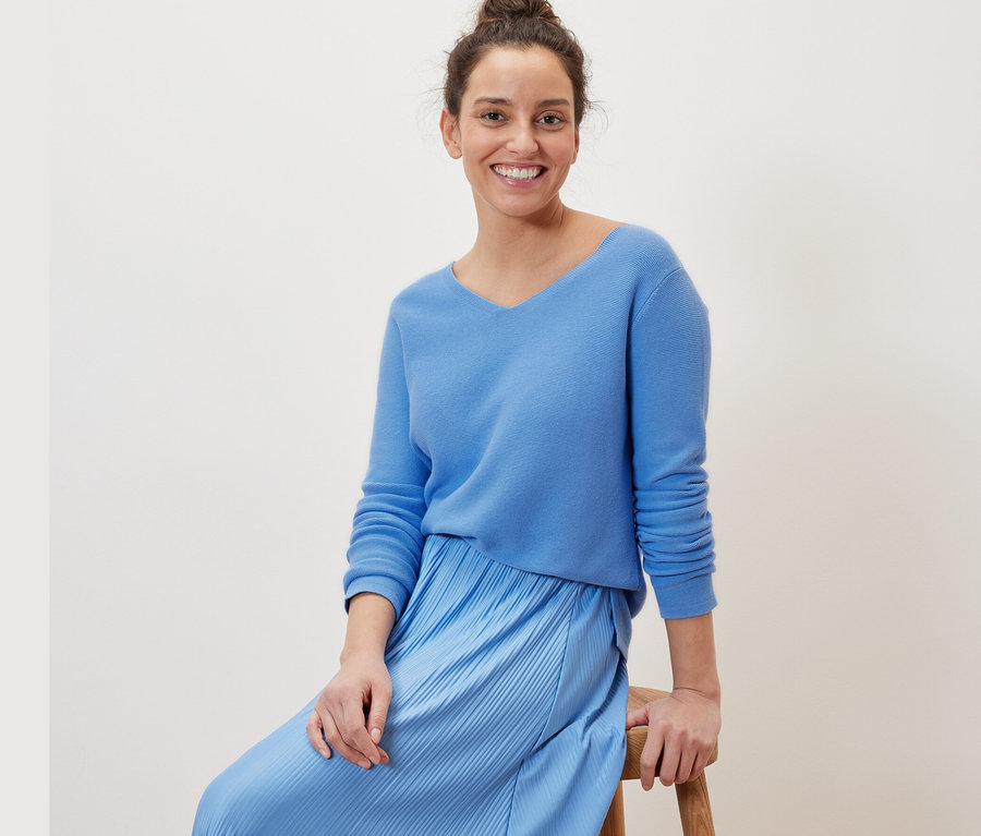 Frau sitzt auf einem Hocker und trägt einen hellblauen Strickpullover.