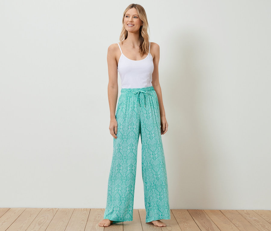 Frau steht und trägt ein weißes Top und eine Relaxhose.