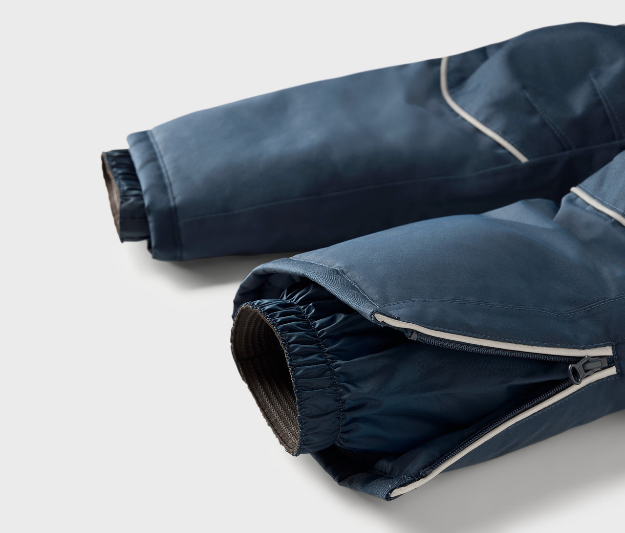 Detailaufnahme einer blauen Skihose mit Reißverschluss am Bein und reflektierendem Streifen.