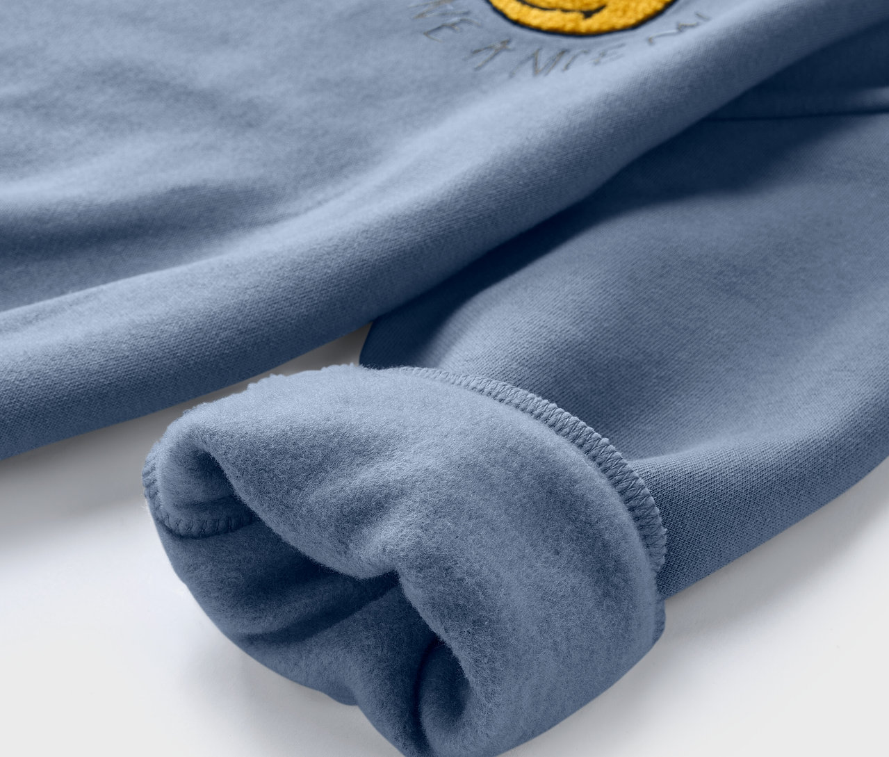 Detailansicht eines blauen Kinder-Sweatshirts SMILEYWORLD® mit angerauter Innenseite und gelbem Smiley.