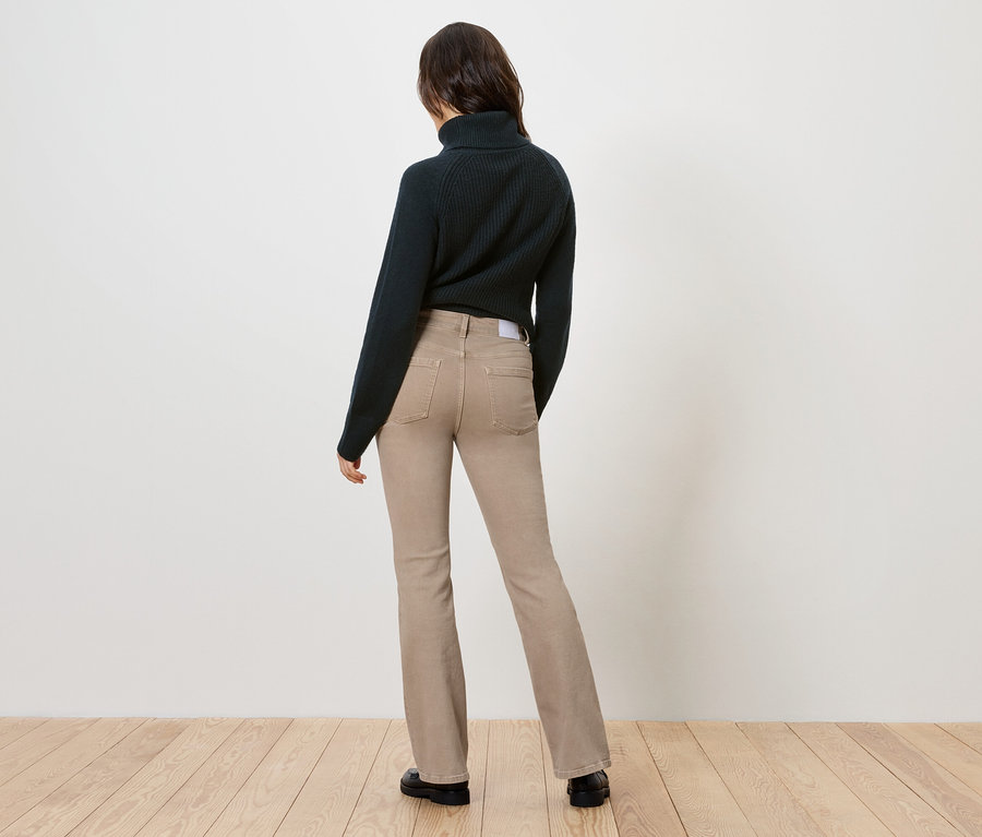 Rückansicht einer Frau mit dunklem Rollkragenpullover und beigen Schlagjeans.