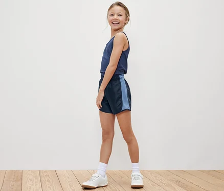 Lächelndes Mädchen posiert in Tanktop und einer der 2 Kinder-Sportshorts.