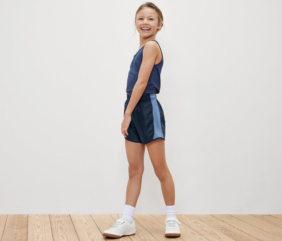 Lächelndes Mädchen posiert in Tanktop und einer der 2 Kinder-Sportshorts.