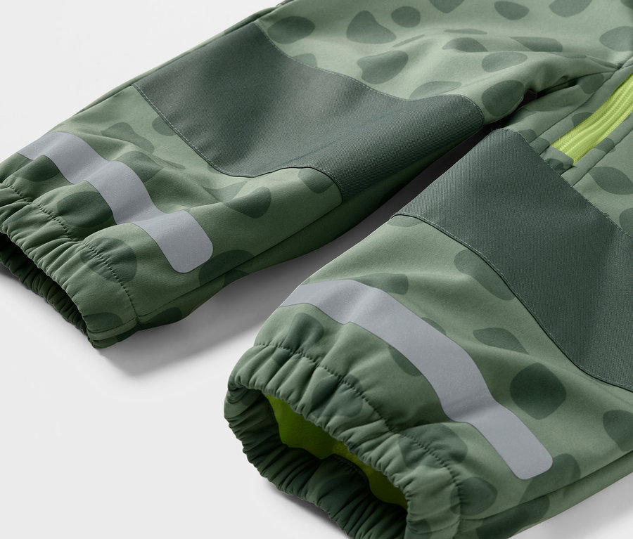 Detailansicht eines Kinder-Softshell-Einteilers mit grünem Tarnmuster, Reflexstreifen und elastischen Bündchen.
