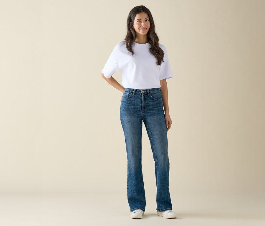 Frau in weißem T-Shirt und blauen Jeans steht und posiert.