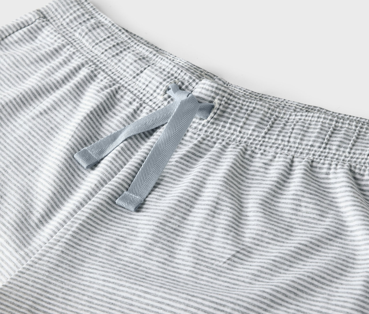 Detail einer grau-weiß gestreiften Hose mit blauem Kordelzug in der Taille.