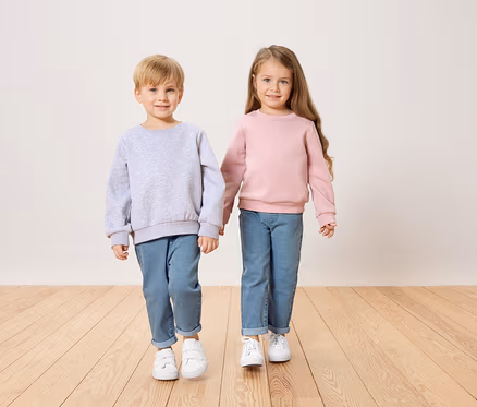 Ein Junge im grauen Pullover und ein Mädchen im rosa Pullover halten Händchen.
