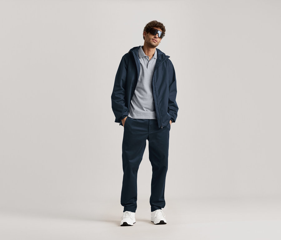 Ein Mann steht mit Sonnenbrille, marineblauer Jacke und marineblauer Chino.