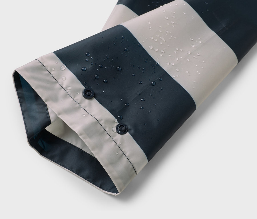 Ärmel einer blau-weiß gestreiften Regenjacke mit Wassertropfen und zwei Druckknöpfen.