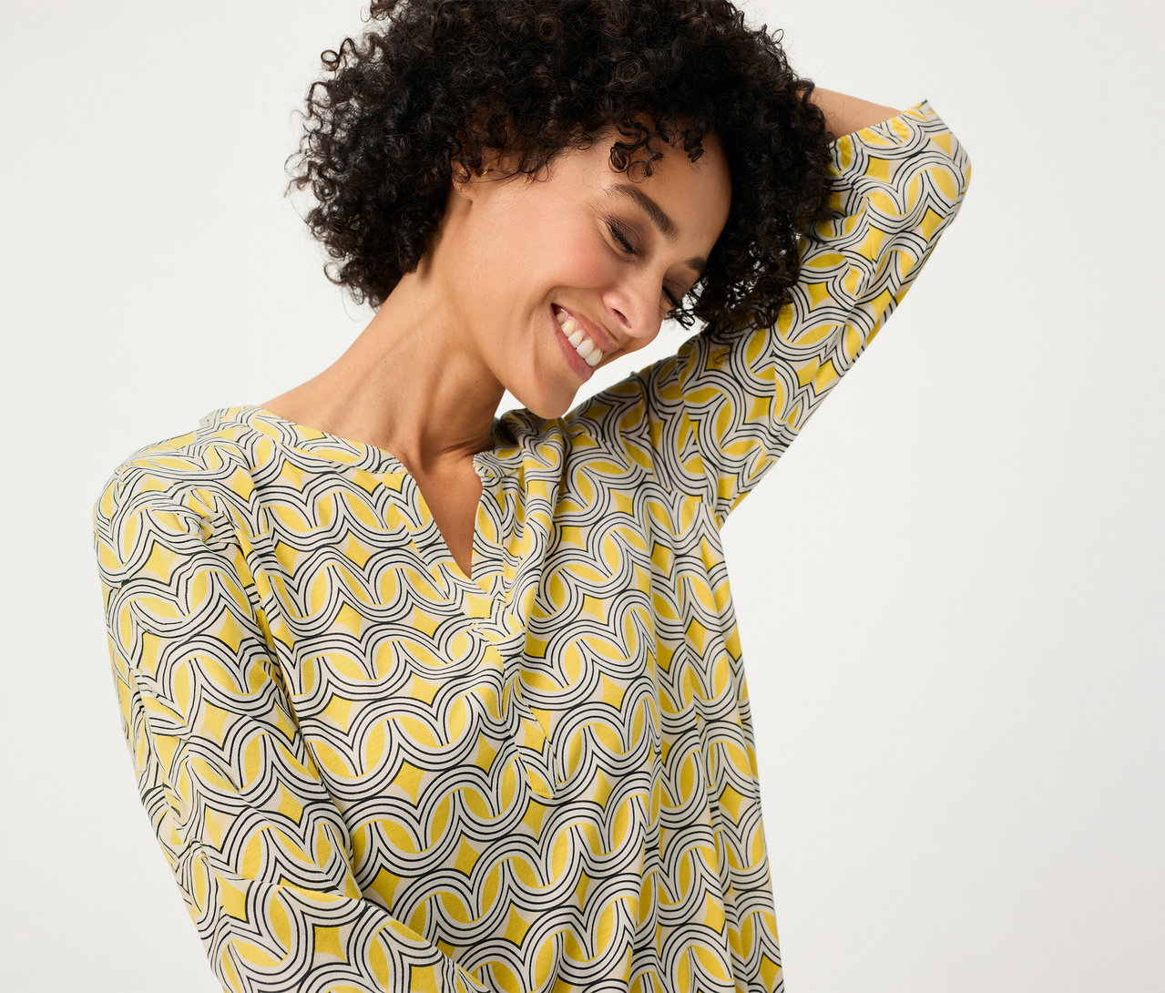 Frau lächelt und trägt ein gelb gemustertes Olsen 3/4-Blusenshirt.