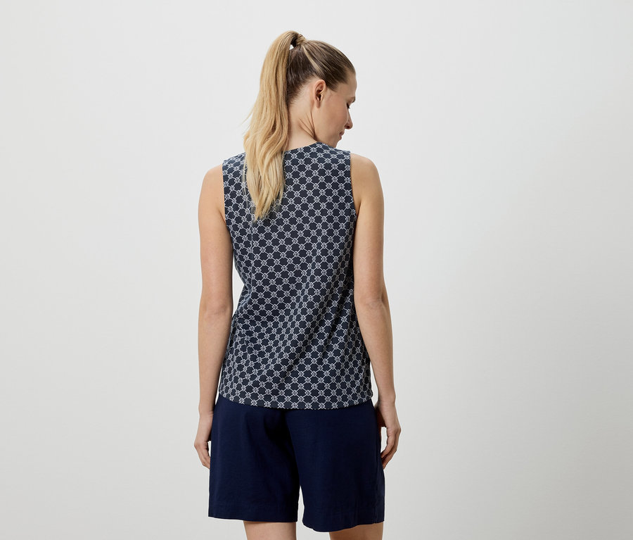 Rückansicht einer Frau mit blondem Haar, die ein blaues, ärmelloses Top mit einem weißen geometrischen Muster und marineblaue Shorts trägt.