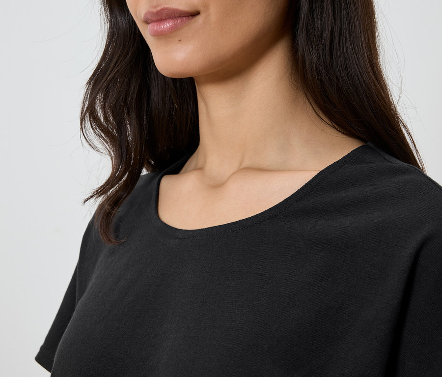 Nahaufnahme einer Frau mit dunklen, gewellten Haaren, die ein schwarzes T-Shirt trägt.