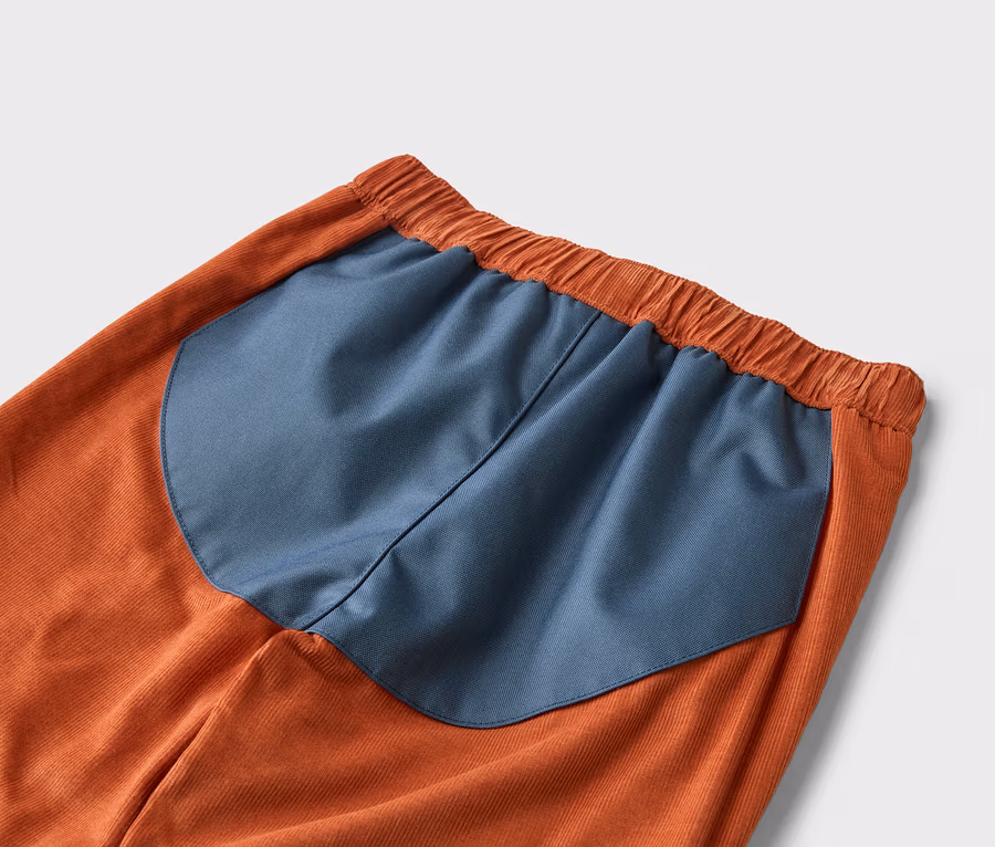Nahaufnahme einer orangefarbenen Kordhose mit einem marineblauen Einsatz am Bund.