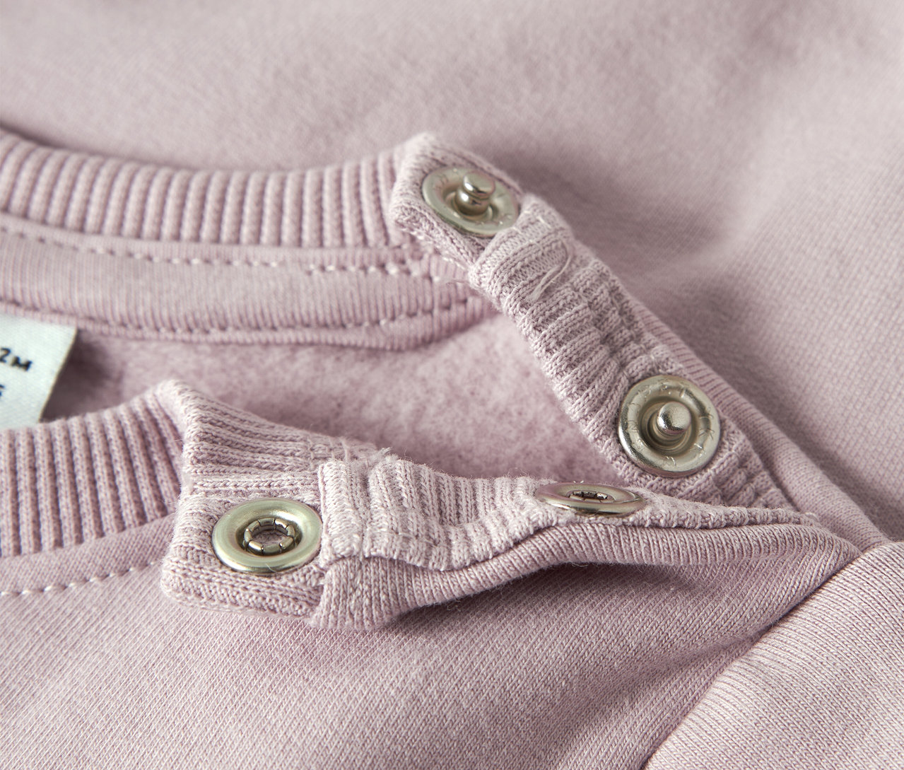 Nahaufnahme eines rosafarbenen NAME IT Baby-Sweatshirts mit Druckknöpfen am Kragen.