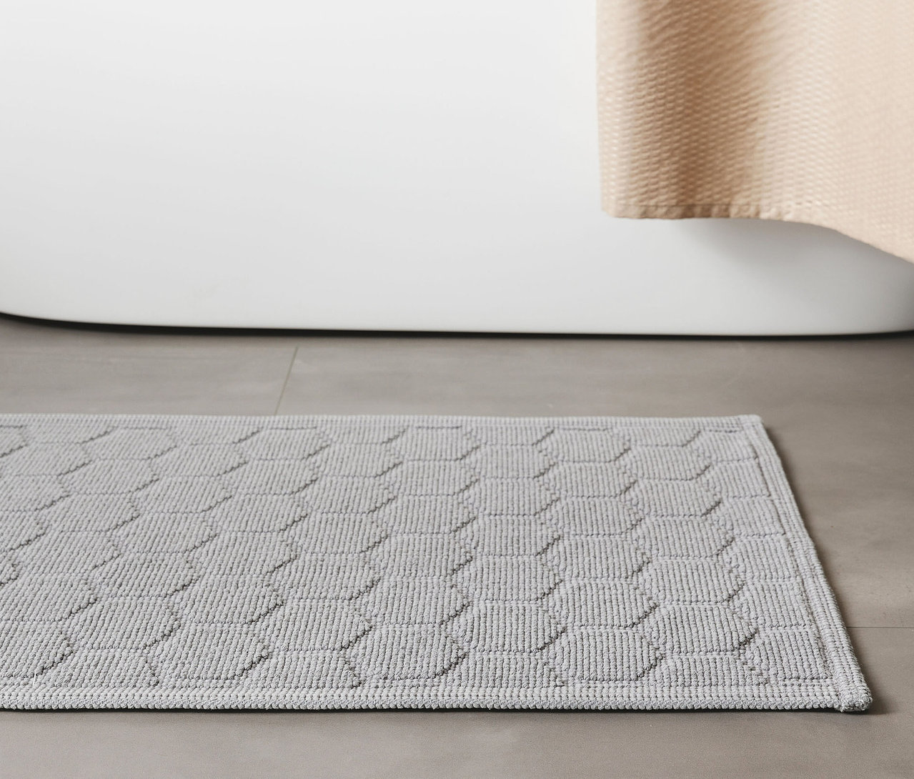 Hellergraue Badematte »Jojo« von benuta mit Rautenmuster, Größe 50 x 80 cm, liegt vor einer Badewanne auf grauem Fliesenboden.