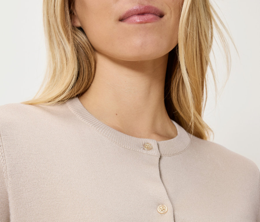 Nahaufnahme einer blonden Frau, die eine beige Strickjacke trägt.