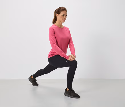 Frau in pinkem Oberteil und schwarzen Leggings dehnt sich.