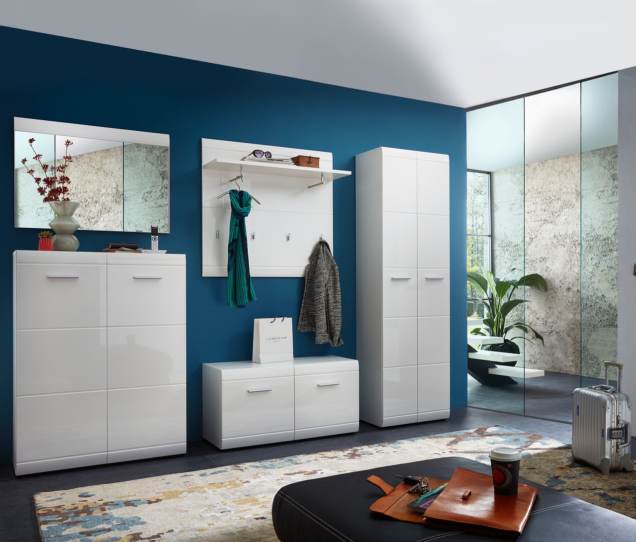 Flur mit breitem, weißen Garderobenpaneel »ADANA«, Schuhschrank, Bank, Spiegel und Schrank vor einer blauen Wand.