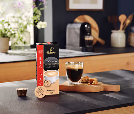 Auf einer Küchentheke stehen eine Packung Cafissimo Decaffeinato Kapseln, eine Tasse Kaffee und eine Kapsel.