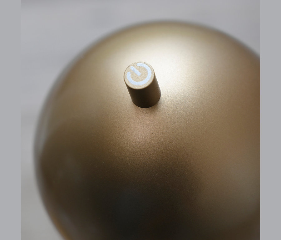 Nahaufnahme einer goldenen, kugelförmigen Oberfläche mit einem kleinen, zylindrischen Knopf darauf, der ein weißes Einschaltsymbol zeigt.