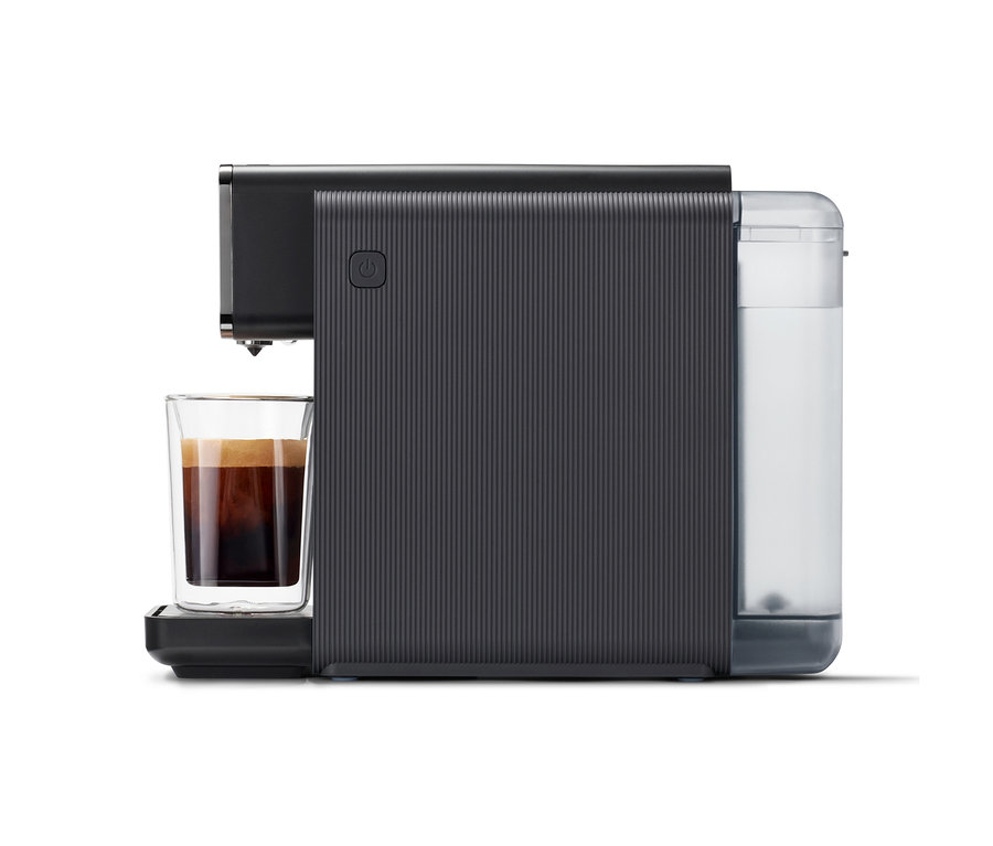Schwarze "Qbo ONE" Kapselmaschine, Soft Black, mit gerippter Textur, die Kaffee in ein Glas füllt. Rechts ist ein teilweise gefüllter Wassertank zu sehen.