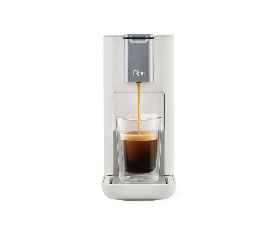 Kaffee läuft aus der Qbo ESSENTIAL Bright Sand Kaffeemaschine in ein Glas.