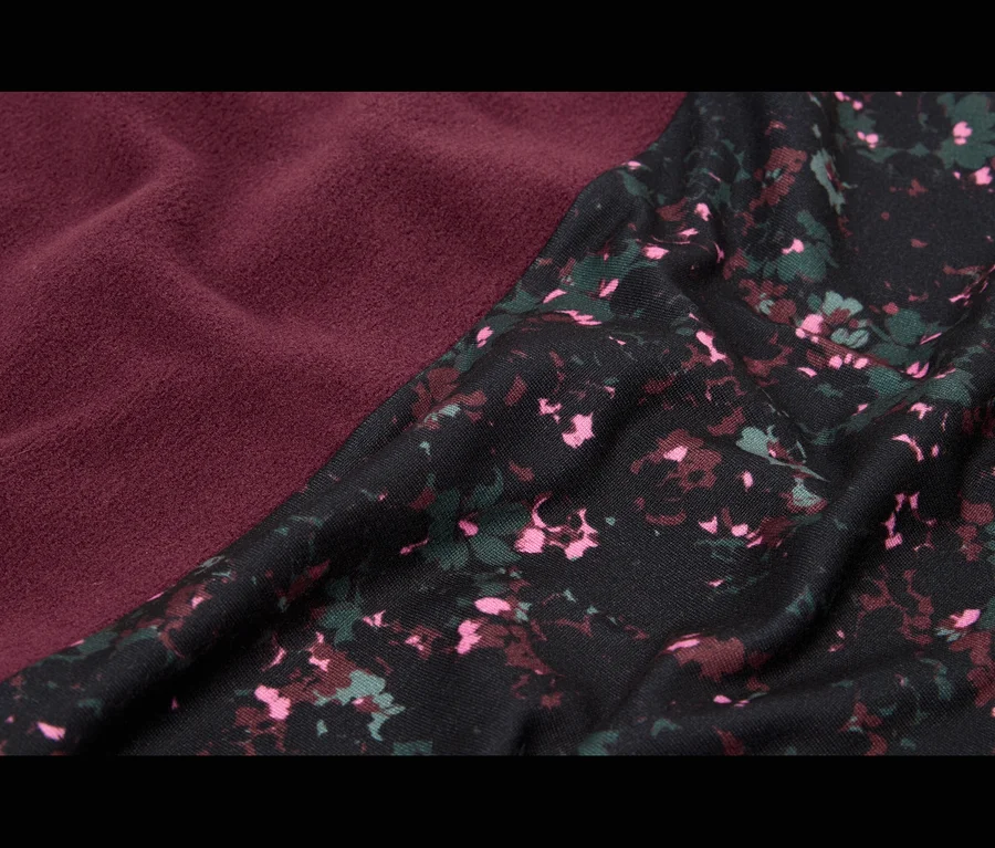 Nahaufnahme von zwei diagonal aufeinandertreffenden Stoffen; einer ist ein strukturierter, burgunderroter Stoff, der andere ist schwarz mit einem verstreuten Blumenmuster in Pink, Dunkelrot und Grün.