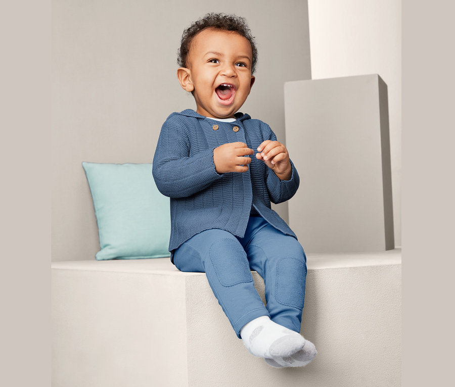 Lächelndes Baby sitzt und trägt eine blaue Strickjacke.