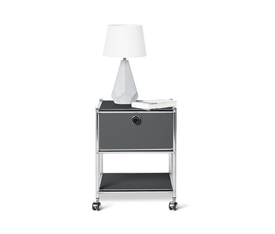 Ein grauer Beistelltisch Metall »CN3« mit Schublade, auf dem eine weiße Lampe und ein Buch stehen.