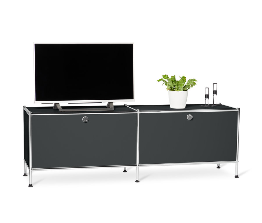 Schwarzes Lowboard Metall »CN3« mit Klappenfächern. Auf dem Lowboard stehen ein Fernseher, eine Topfpflanze und zwei Kerzenständer.