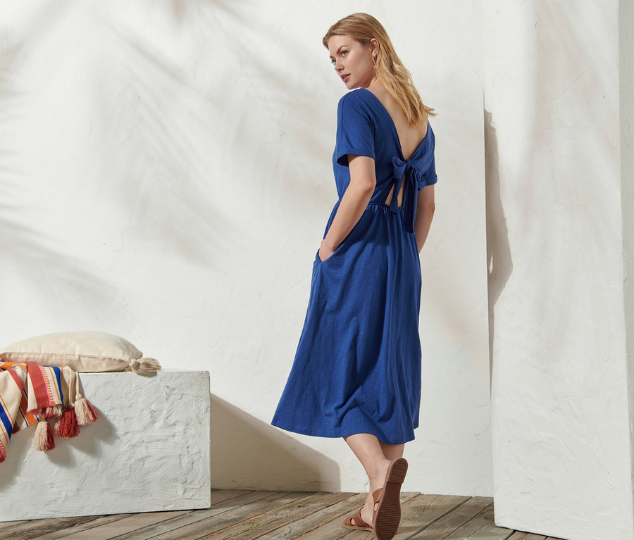 Frau steht seitlich und trägt ein blaues Jerseykleid mit Rückenausschnitt.