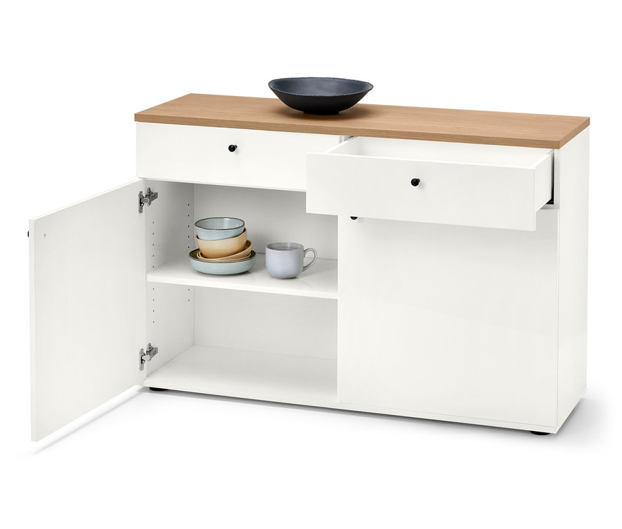 Weiße Kommode mit Holzplatte, offenem Schrank mit Tellern und Tasse und ausgezogener Schublade.