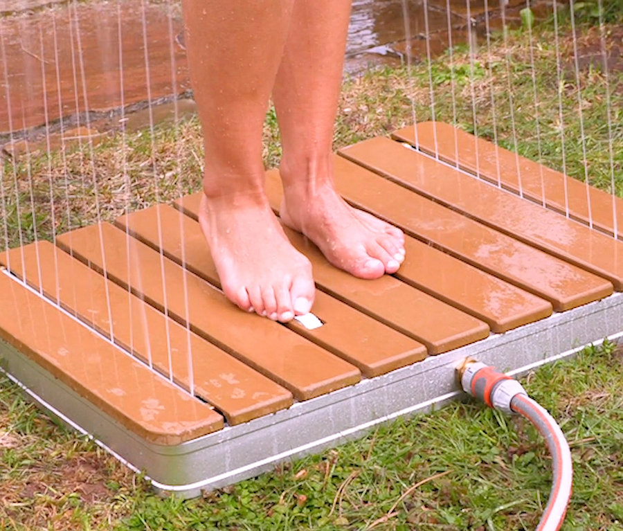 Füße stehen auf der Breuer®-Outdoor-Bodendusche »Fontana«, aus der Wasser sprüht.